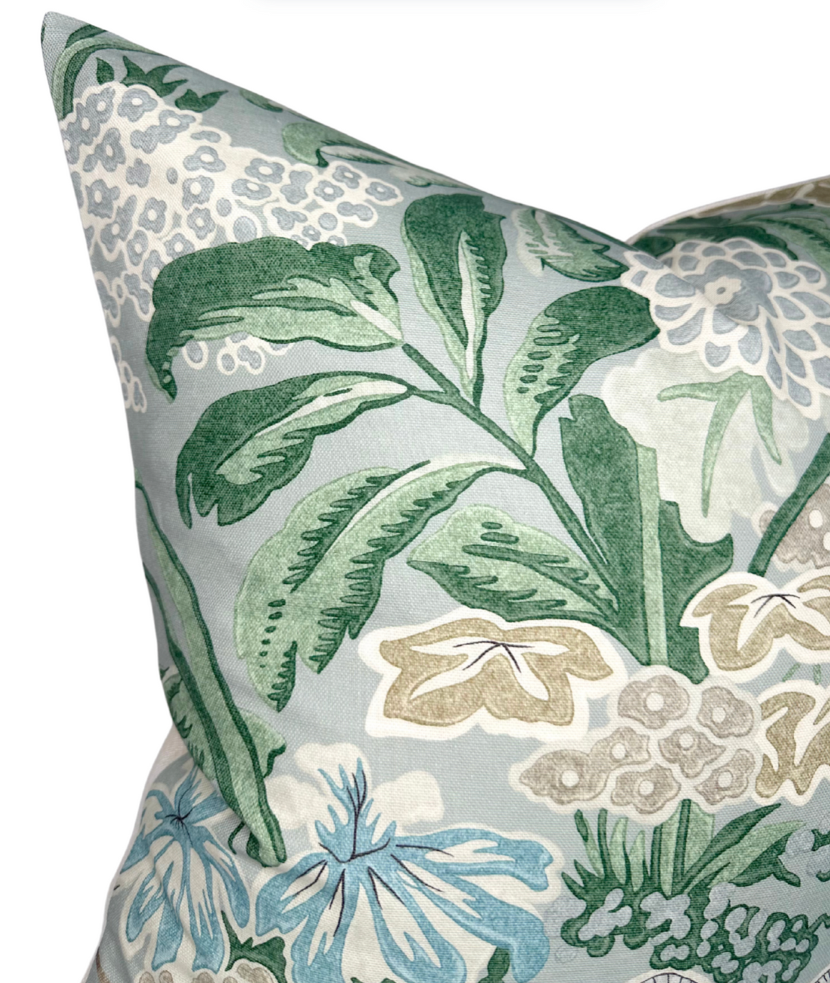 Close-up of a pillow with sage green and blue floral patterns on a soft gray background, featuring detailed leaves and clustered blossoms.