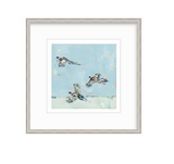 Art print depicting three pheasants flying against a soft blue and white abstract background in a light wood frame with a white mat.