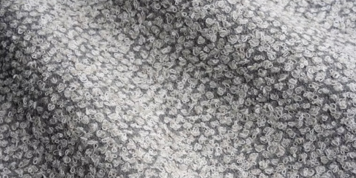 Close-up of a woven pillow cover fabric showing a dense pattern of small, irregular platinum-colored loops with subtle shading variations creating a textured effect.