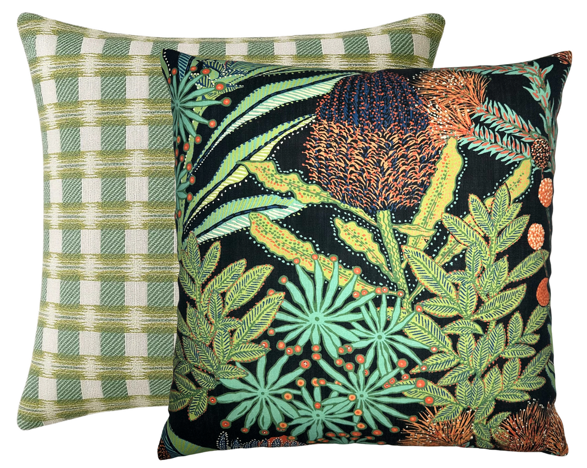 Two square pillows with distinct covers: front pillow has a vivid black background with detailed green and orange protea flower and leaf pattern; back pillow shows a green and white checkered pattern.