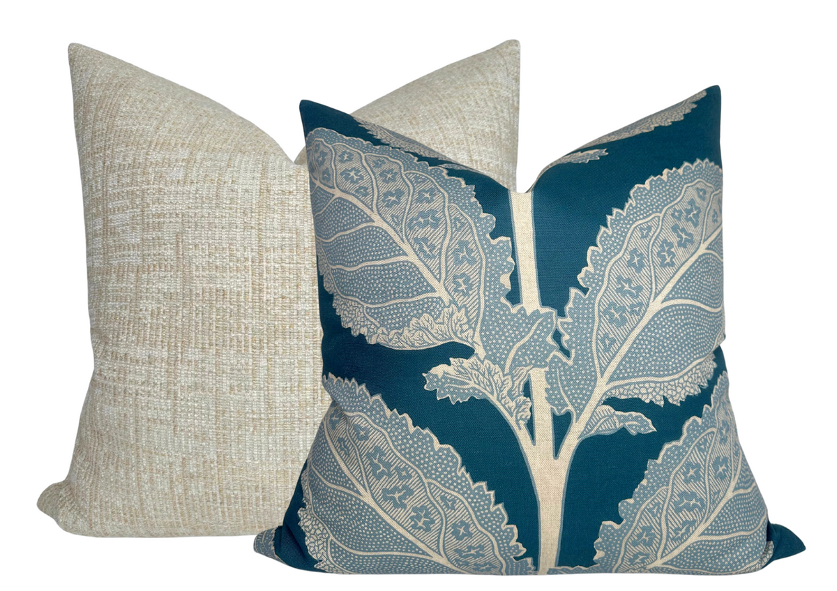 Two square pillows, one with a large blue and cream leaf pattern and the other with a textured beige woven fabric, shown side by side against a white background.