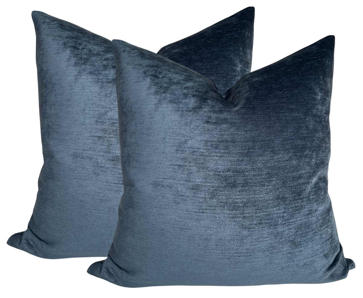 Two sapphire blue velvet pillow covers with a soft, slightly shiny texture and a plush, square shape shown against a white background.