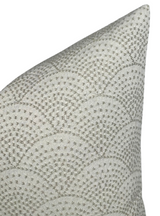 Corner of a woven pillow cover displaying a scalloped pattern in natural beige and light gray tones with textured fabric.