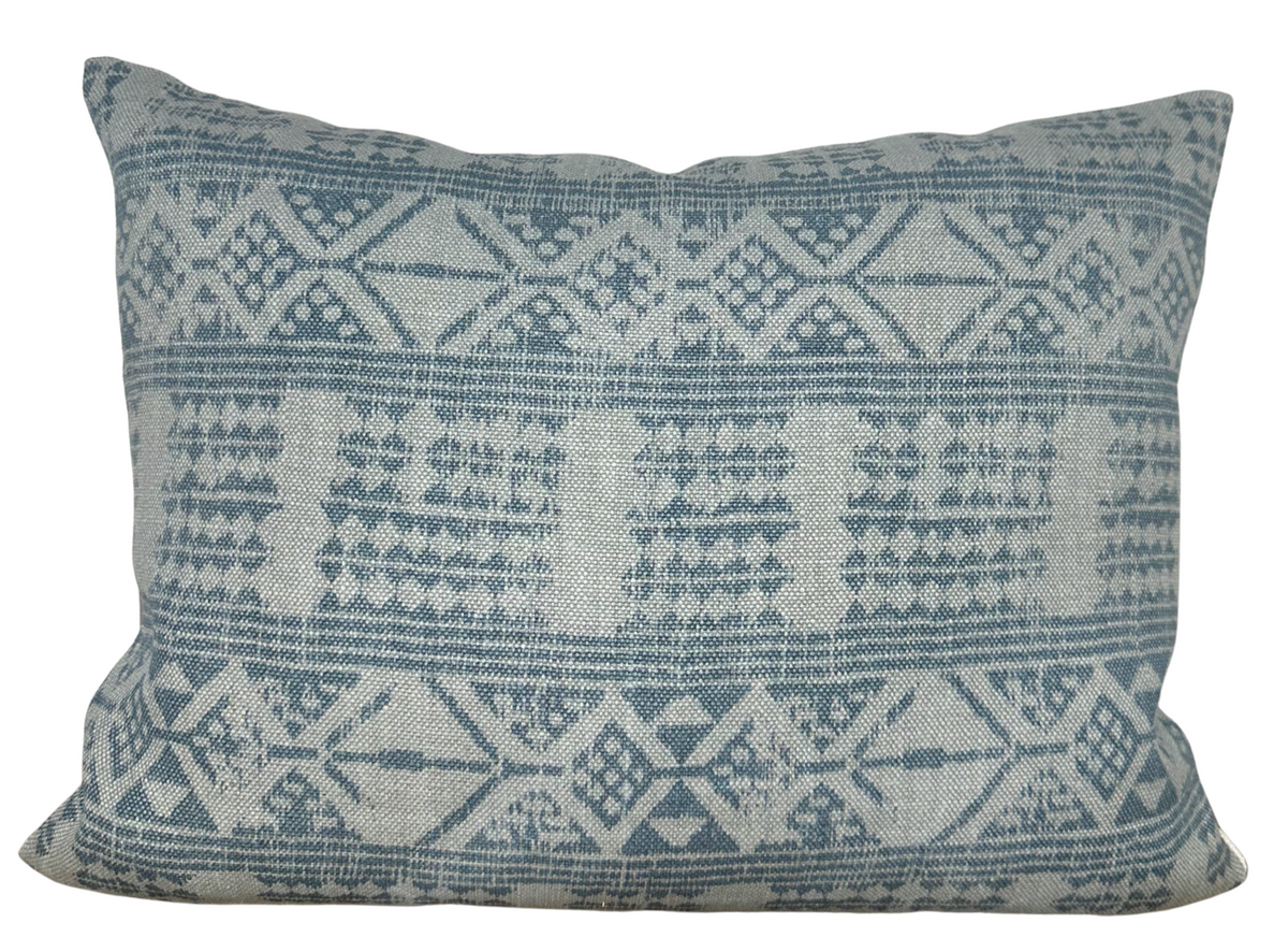 Rectangular pillow cover featuring a woven geometric pattern in muted blue and off-white tones with diamond and triangular shapes across its surface.