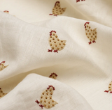 Ivory-colored fabric with a woven pattern of small chickens in tan with red combs and feet, shown in soft folds.