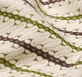 Close-up of fabric with repeating abstract leaf-like pattern in olive green and dark brown on a cream background, showing texture and folds.
