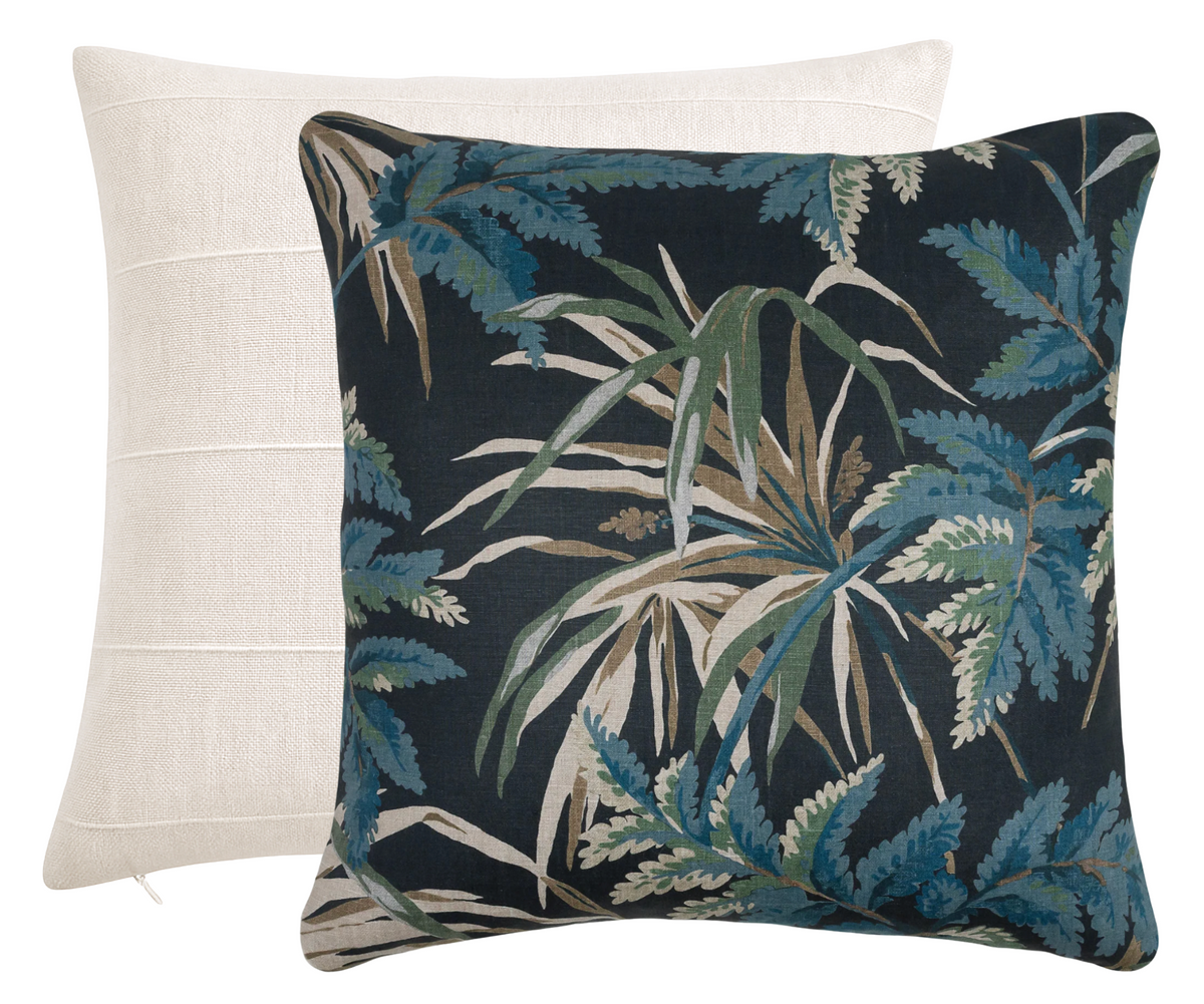 Two square pillow covers stacked, one solid sandstone beige with subtle horizontal seam lines, the other black with blue, green, and beige tropical leaf pattern.