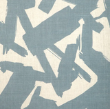 Close-up of linen fabric with abstract bold brushstroke patterns in muted blue on a natural beige background, showing fabric texture and irregular shapes.
