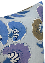 Close-up of a pillow corner with a natural linen background and a floral pattern featuring blue, lavender, and brown petals outlined in black.