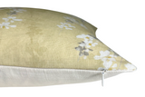 Close-up side view of a gold fabric pillow cover with a subtle floral print in white and gray, featuring a white zipper along the bottom edge.