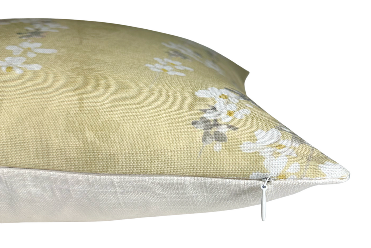 Close-up side view of a gold fabric pillow cover with a subtle floral print in white and gray, featuring a white zipper along the bottom edge.