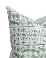 Green geometric pattern of squares and diamonds on off-white fabric pillow cover, shown close-up with two corners overlapping.