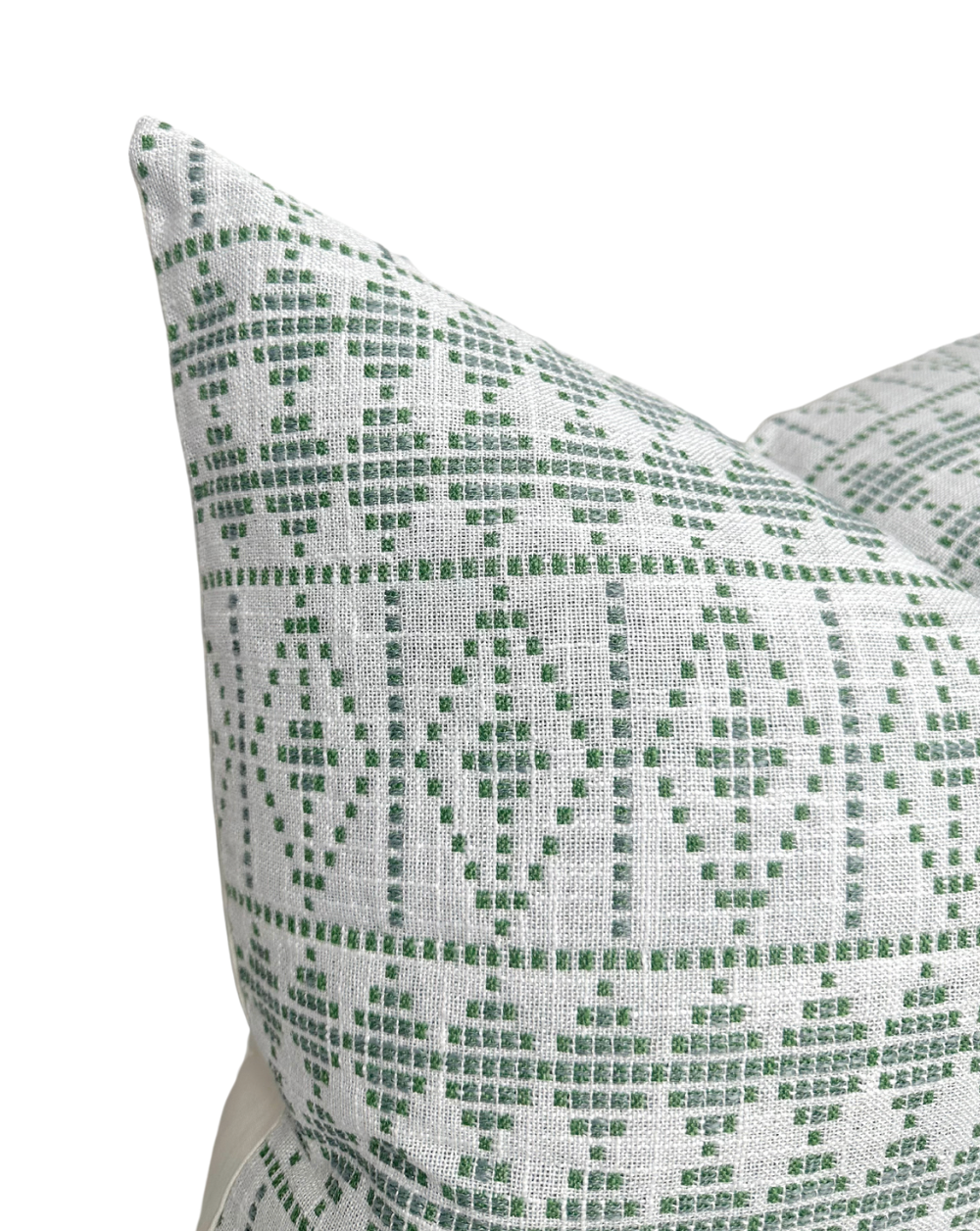 Green geometric pattern of squares and diamonds on off-white fabric pillow cover, shown close-up with two corners overlapping.