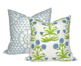 Two square pillows with floral patterns, one featuring blue chamomile flowers with green stems on white, the other a soft blue geometric print on white.