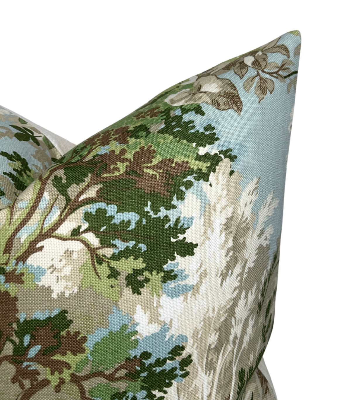 Corner of a fabric pillow cover featuring a detailed toile pattern with green and brown tree branches and white foliage on a light blue background.