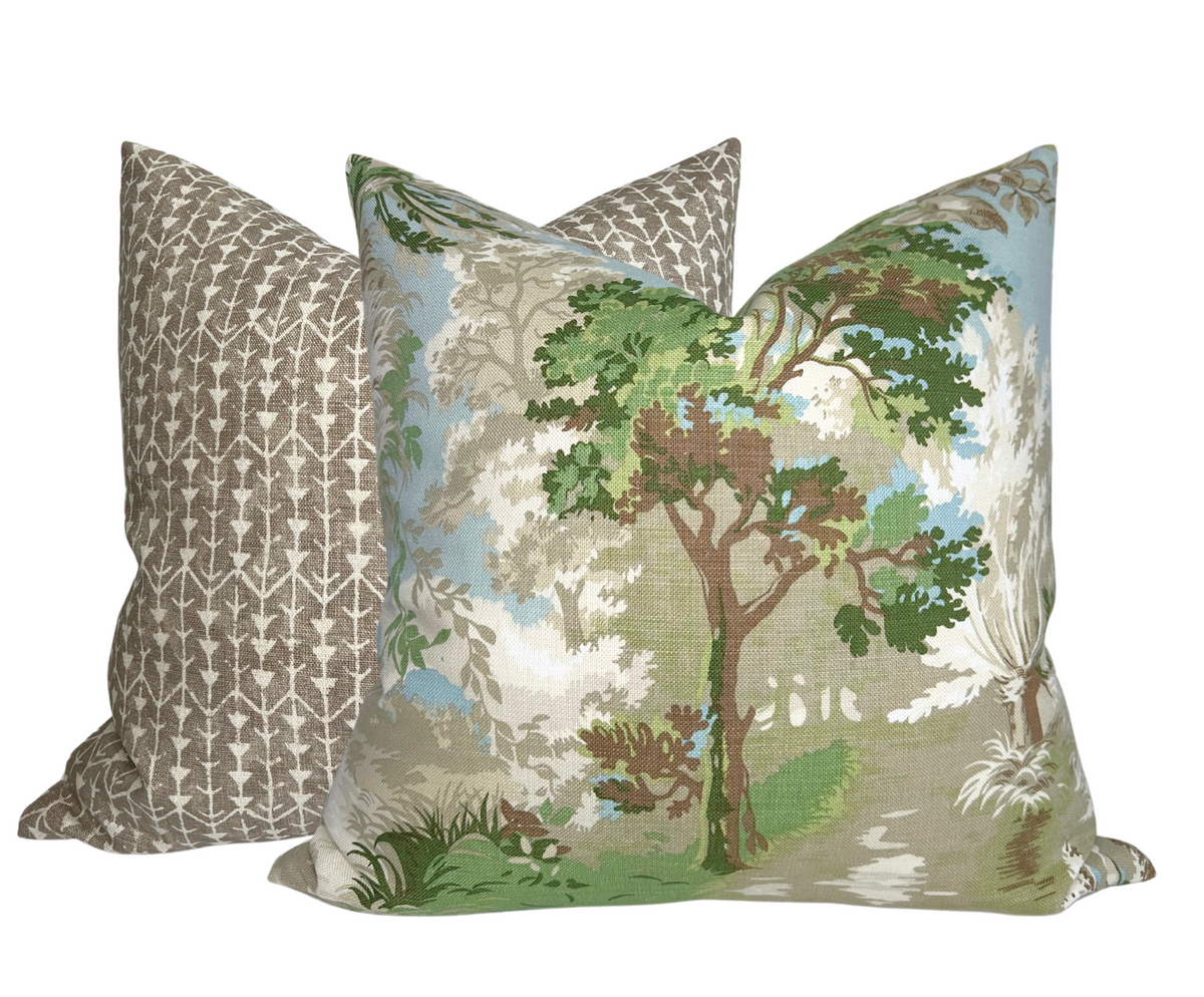 Two square pillows, one with green and blue toile print featuring trees and foliage, the other with a simple beige and white geometric pattern.