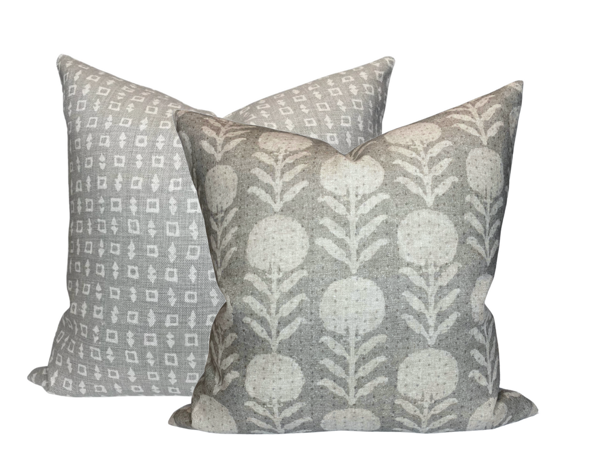 Two square pillows with sand grey fabric, one featuring a repetitive white geometric pattern and the other with a white stylized floral design.