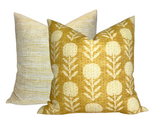 Two square pillow covers, one with a goldenrod background and white zinnia flower pattern, the other with a subtle striped woven texture in complementary light shades