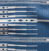 Close-up of a woven textile in indigo blue with horizontal rows of elongated white shapes and diamond motifs, showing subtle fabric texture and natural wrinkles.