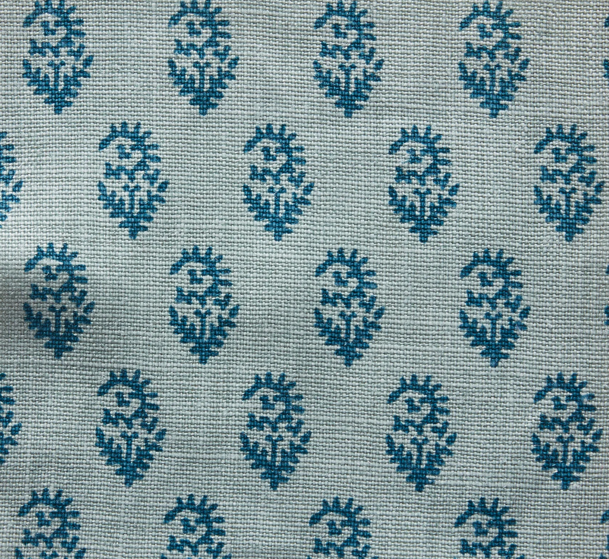 Fabric with a repeated blue organic-shaped block print pattern on a light blue woven background, showing visible thread texture.