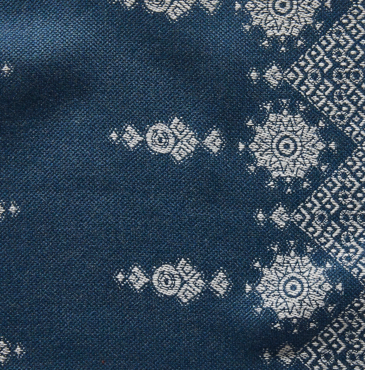 Indigo fabric with white geometric and floral patterns, including circular medallions and diamond shapes along one edge.
