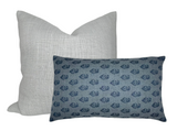 Two pillows, one square in light gray linen texture behind one rectangular in blue with a small dark blue floral pattern, shown against a white background.