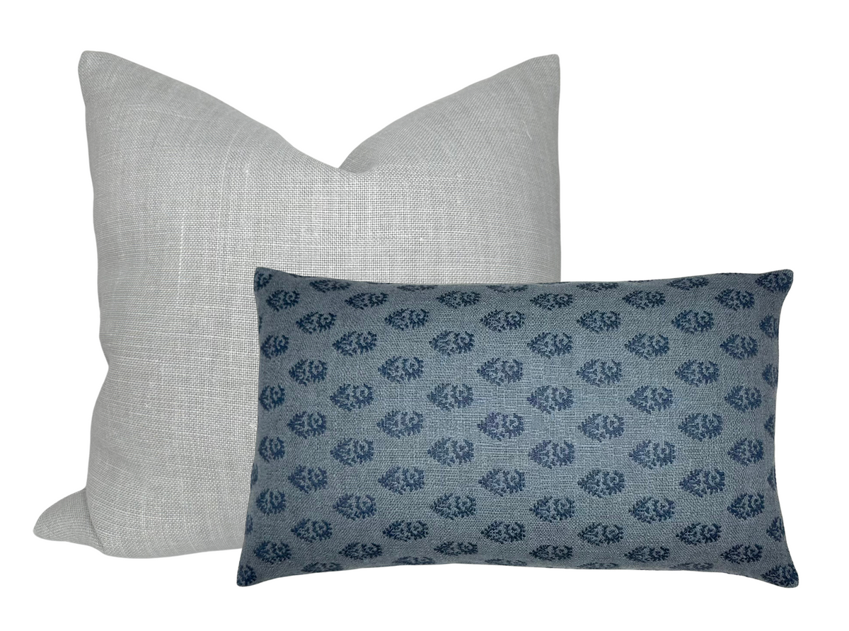 Two pillows, one square in light gray linen texture behind one rectangular in blue with a small dark blue floral pattern, shown against a white background.