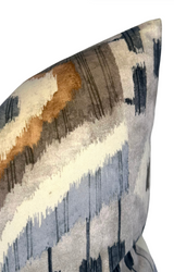 Close-up of a velvet pillow cover with abstract brushstroke patterns in shades of brown, gray, blue, and cream, showing soft texture and gradient detailing.