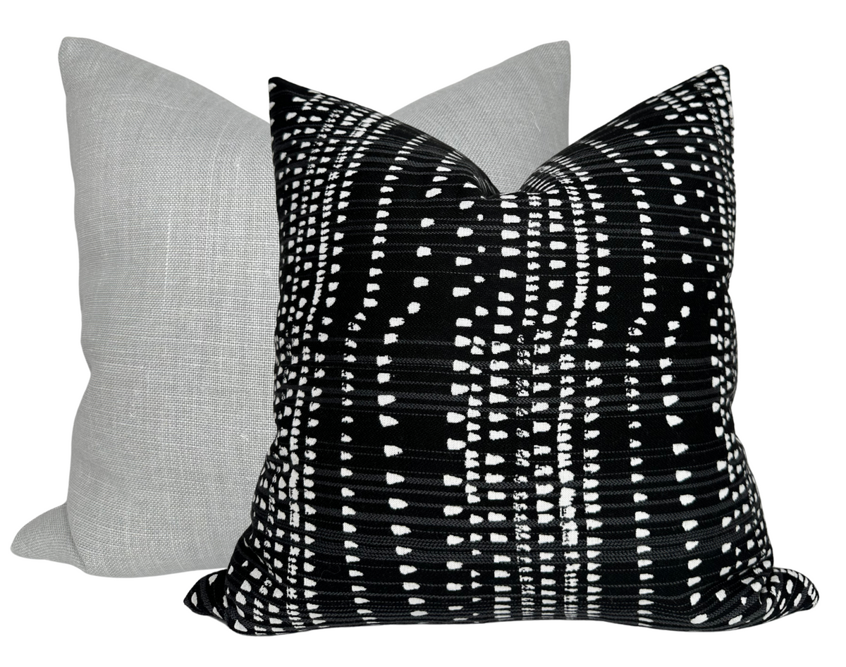 Two square pillows with knife edges, one in solid light gray linen fabric and the other in black fabric patterned with white irregular horizontal and vertical lines forming a modern geometric design.