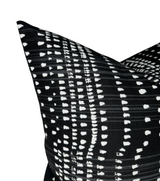 Close-up of a black pillow cover with white irregular dotted and dashed vertical lines creating a linear pattern, showing textured fabric and sharp corner details.