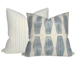 Two textile pillow covers, one with vertical beige and white stripes and the other with blue geometric inlay pattern on a natural background, arranged overlapping.