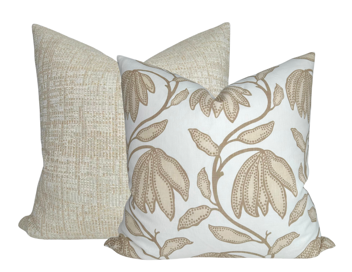 Two square pillows with a beige natural woven texture on one and a white fabric with tan floral vine pattern on the other, arranged side by side.