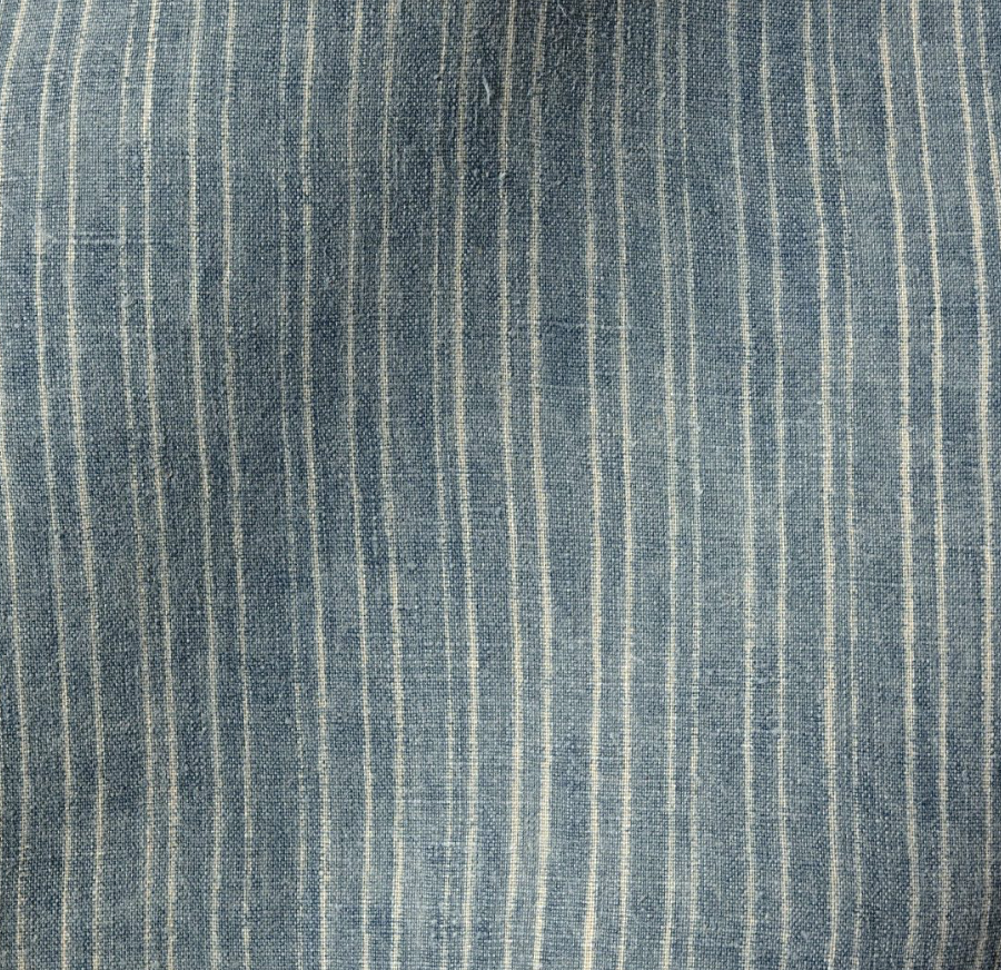 Close-up of fabric with vertical off-white pinstripes on a soft, washed aurora blue background, showing subtle texture and light natural creases.