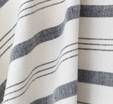 Natural-colored fabric with alternating thick and thin black horizontal stripes, showing woven texture and soft draping folds.