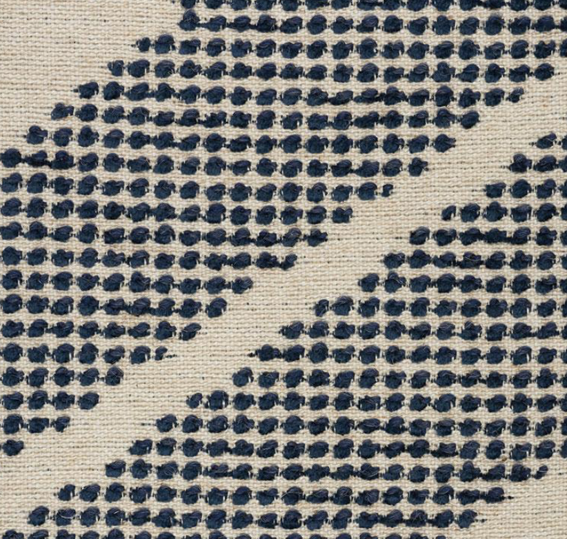 Close-up of woven off-white fabric with diagonal rows of clustered indigo blue dots forming a textured geometric pattern.