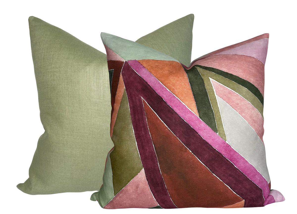Two square pillows, one solid muted green and the other with abstract geometric pattern in rose, burgundy, olive, and blush tones with velvet texture.