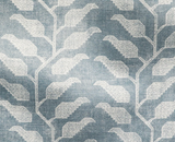 Textile with a geometric leaf pattern in white and lake blue, showing a textured woven fabric with repeating stylized branches and angular leaves.