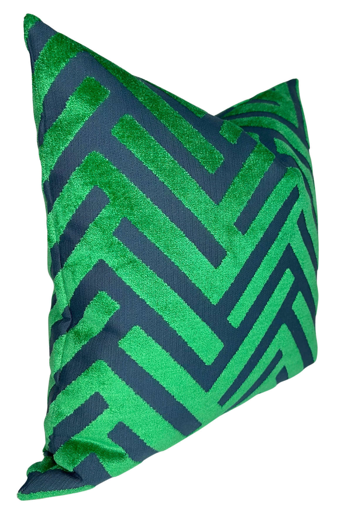 Square pillow cover with a geometric zigzag pattern in emerald green cut velvet on a dark blue fabric background, shown at an angle.