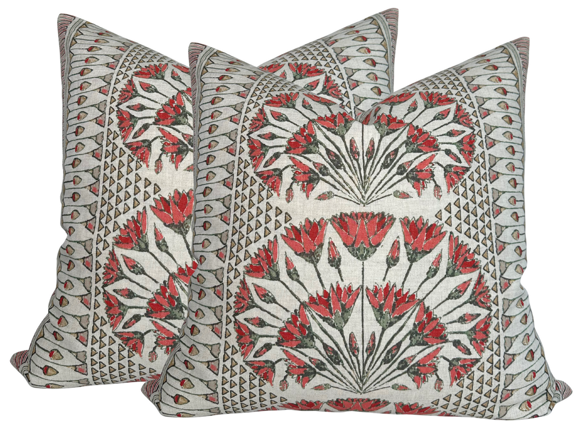 Two square pillow covers with coral and black floral patterns arranged in fan shapes on a beige background with geometric border designs.