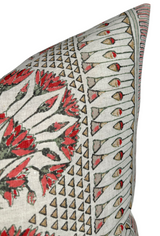 Corner of a beige pillow cover with a red floral and geometric pattern featuring triangles and stylized red-tipped shapes on a textured fabric.
