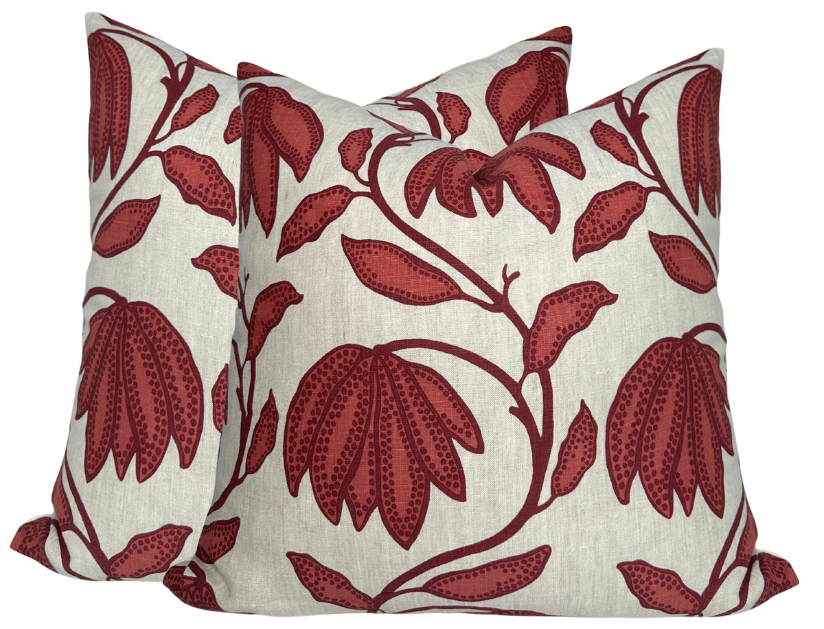 Two square pillows with a cream background and a bold floral design featuring large sunbaked red petals and leaves connected by thin red branches.