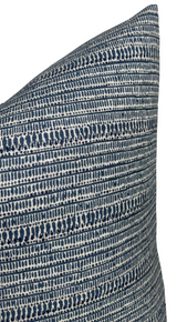 Close-up of a pillow cover with horizontal patterns of dark blue and white stripes resembling woven texture, showing the top corner detail.