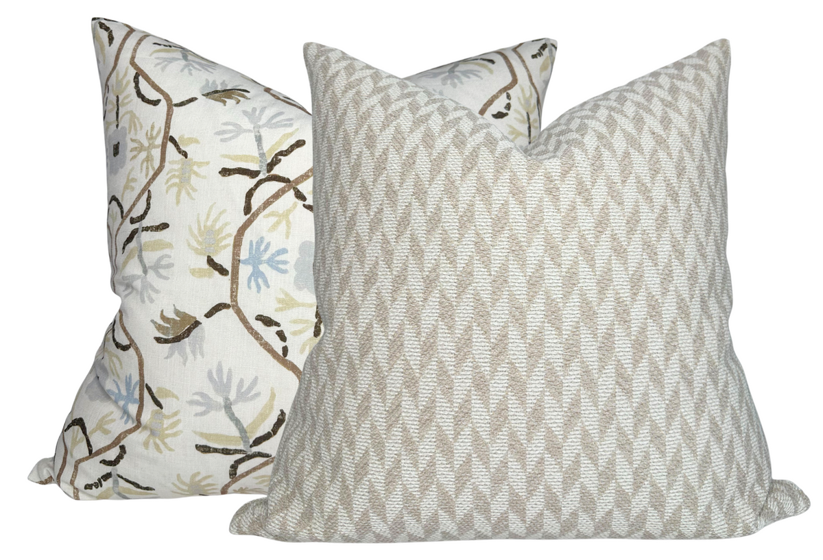 Two pillows, one with tan and white woven geometric pattern, the other with cream fabric featuring brown and blue botanical branch design, side by side.