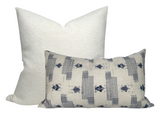 Two pillows with woven texture; a larger square pillow in solid off-white and a smaller rectangular pillow with a blue and off-white striped pattern.