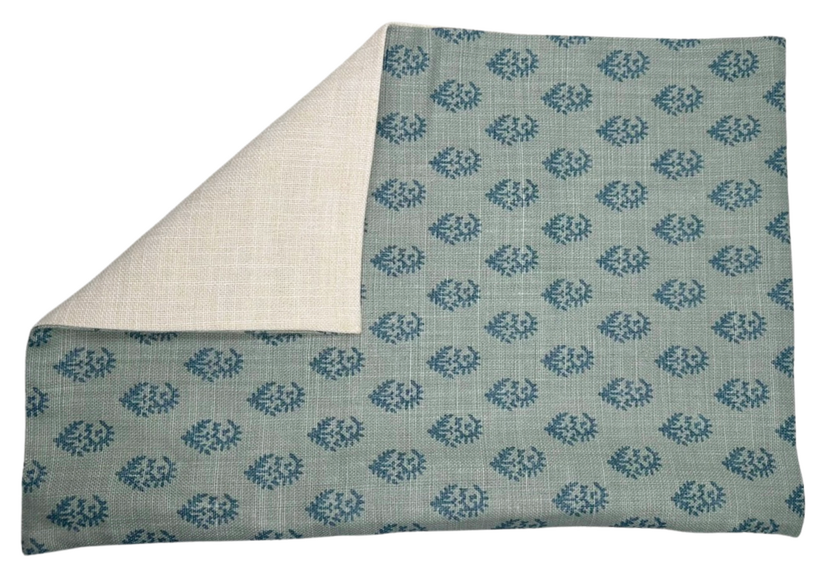 Rectangular pillow cover in muted blue with repeating dark blue floral motifs, folded to show its plain beige reverse side with a woven texture.