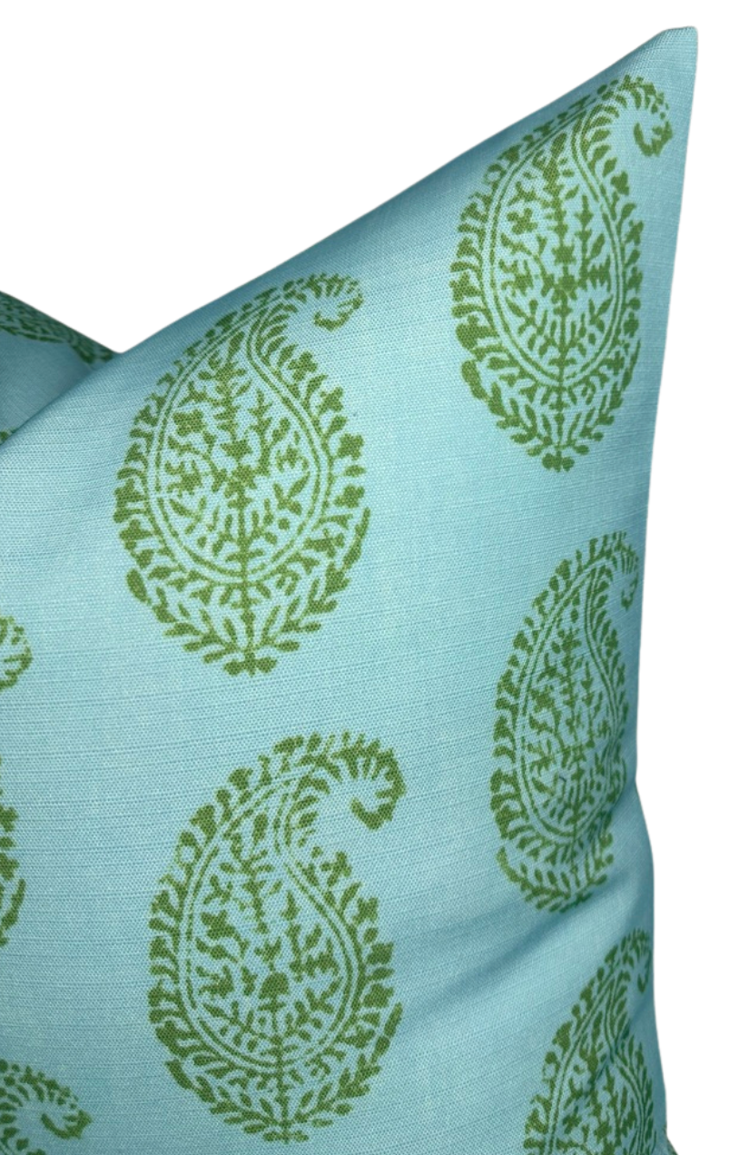Close-up of a blue pillow cover with repeating large green paisley motifs featuring intricate floral details, shown from an angled side view.