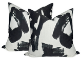 Two square pillow covers with an abstract black brushstroke pattern on a white background, arranged overlapping and viewed from the front.