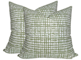 Pair of square pillows with a white background and intersecting green grid pattern in varying thicknesses, shown against a plain white backdrop.
