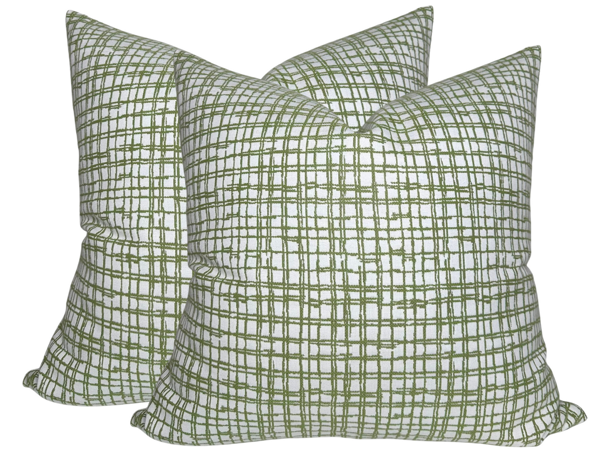 Pair of square pillows with a white background and intersecting green grid pattern in varying thicknesses, shown against a plain white backdrop.