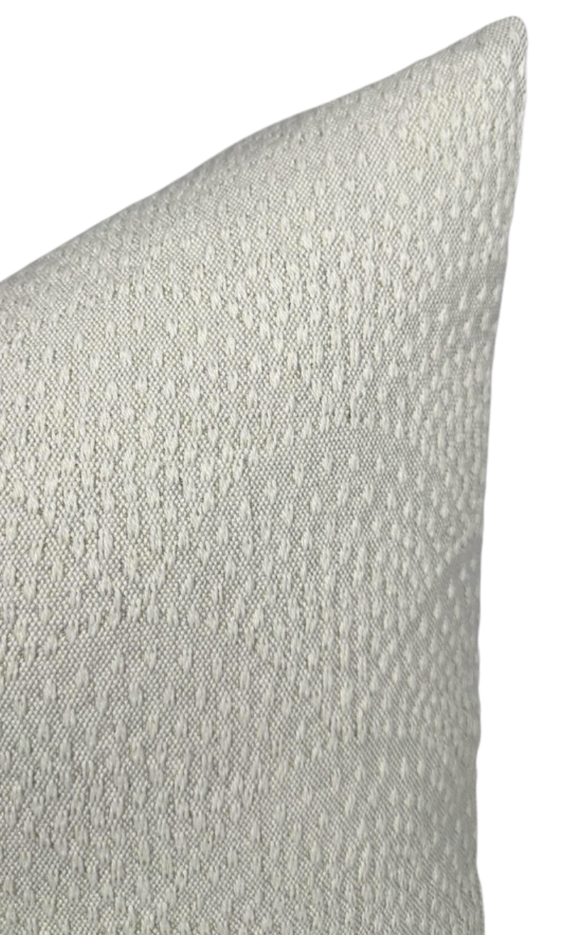 Close-up of a natural-colored woven pillow cover featuring an inverse scalloped texture with raised diamond patterns in soft off-white tones.